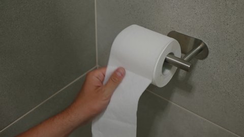 Hand taking toilet paper from a wall mounted toilet paper roll dispenser close up
