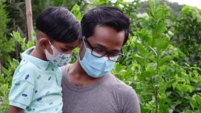 An Asian young and boy wearing safety masks are spending a good time in the green garden. Covid-19 pandemic, Lockdown, and home quarantine time safety concept and educational slow-motion video. 