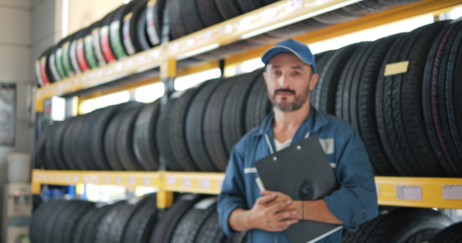 Portrait of smiling mechanic employee in work uniform looking camera at car tires shop service, Specialist tire fitting in the car service, checks the tire and rubber tread for safety. Royalty-Free Stock Footage #1077996098