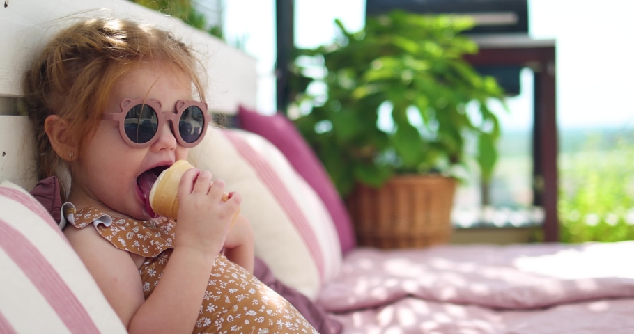 cute toddler baby girl eating ice cream, relaxing on sofa in the garden at warm summer day, proposing you to try some Royalty-Free Stock Footage #1077999968