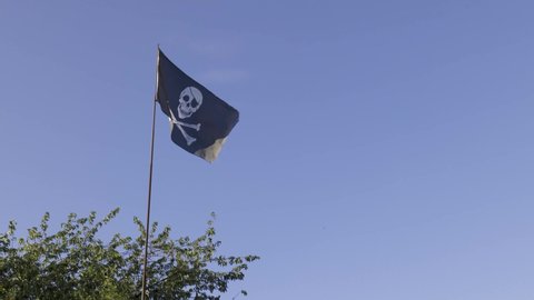 Skull and crossbones pirate flag waving in the wind against a cloudless blue sky.