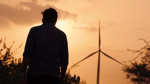 Silhouette of an Indian man walking towards the windmill during the sunset at Wankaner, Gujarat, India. Green Energy background. Environmental conservation concept