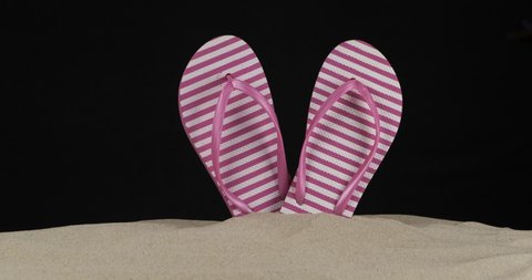 Beach flip flops sticking out of the sand. Slider shot. Isolated. Black background