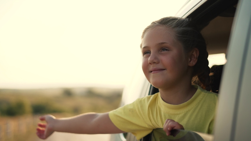 Child in car window. Family car trip. Child hair in wind. Girl looks out of car window. Happy child travel with his family. Girl stretches out his hand to wind. Happy family travel concept by car | Shutterstock HD Video #1078010627