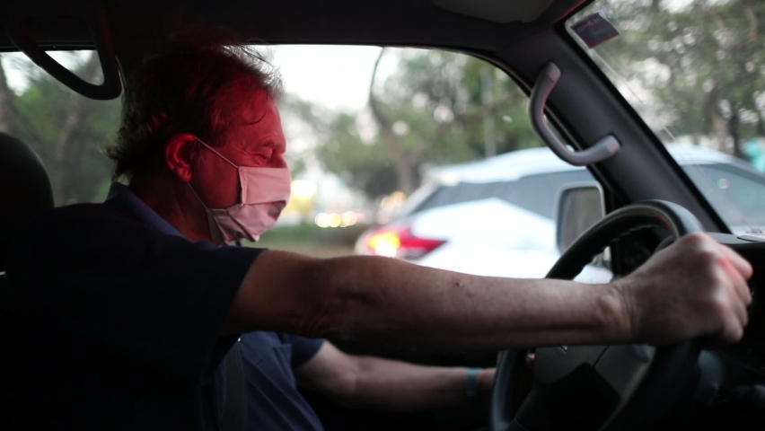 Older man stuck in red light removing covid-19 face mask while stopped in traffic