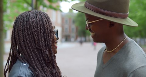 Close up of african young man and woman holding hands and talking outdoors. Cute couple in love cuddle and chat standing on city street