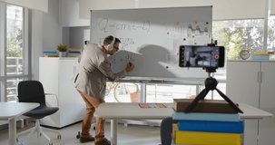 Mature math teacher recording tutorial video for students on smartphone. Professor writing on whiteboard having online broadcast