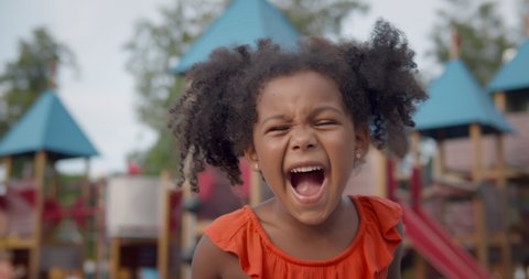 Medium shot of cute afro-american little girl yelling on playground. Portrait of african preschool kid looking at camera and screaming outdoors