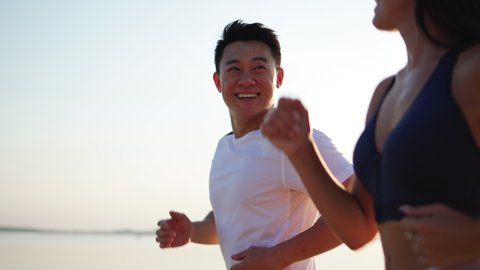 Young joyful active couple jogging together along beautiful beach. Running happy woman and man enjoying their summer morning workout. Team sports.