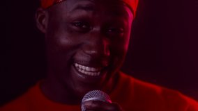 Talented Singer. African American Guy Singing Song Posing With Microphone Looking At Camera Standing In Dark Studio Illuminated With Red Neon Lights. Vocal, Musical Talent. Closeup, Selective Focus