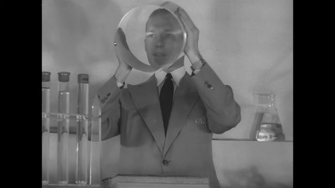 CIRCA 1940s - A DuPont chemist holds up a giant, transparent glass cylinder to his face during a presentation.