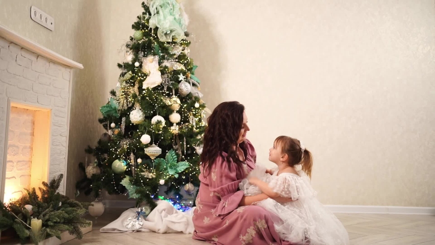 mom and daughter play at the Christmas tree. tradition to spend the New Year holidays with the family. happy childhood. games with children.