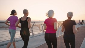 Active lifestyle. Group of healthy mature women wearing sport clothes running together outdoors, warming up early in morning, tracking shot, slow motion