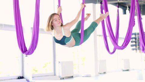 Young beautiful woman practice in aero stretching swing. Aerial flying yoga exercises practice in purple hammock in fitness club.