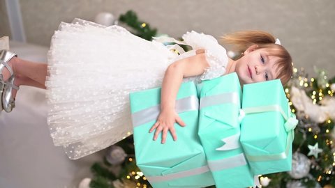 vertical video. a little girl keeps a tower of gift boxes under the Christmas tree and she falls. tradition to give gifts for the new year. festive sale of toys and goods for children.