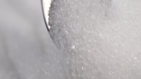 Teaspoon moves in slow motion in the sugar heap and scoops up the shiny white crystals with the spoon. Macro shot.