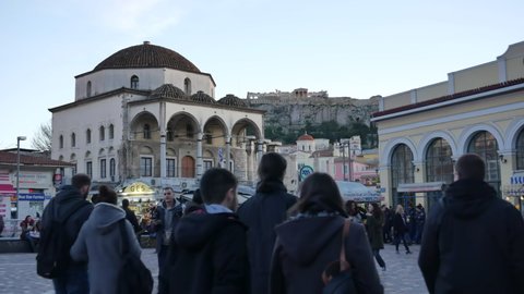 ATHENS - JANUARY 19, 2018: People crowd on Monastiraki Square in Athens at the evening. The view on Tzistarakis Mosque and the Acropolis. Medium shot.