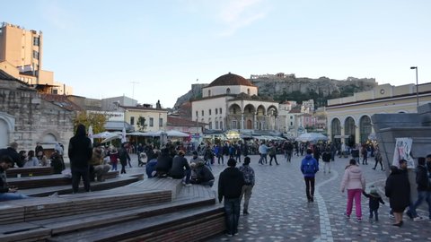 ATHENS - JANUARY 19, 2018: People crowd on Monastiraki Square in Athens at the evening. The view on the Tzistarakis Mosque and the Acropolis. Wide shot.