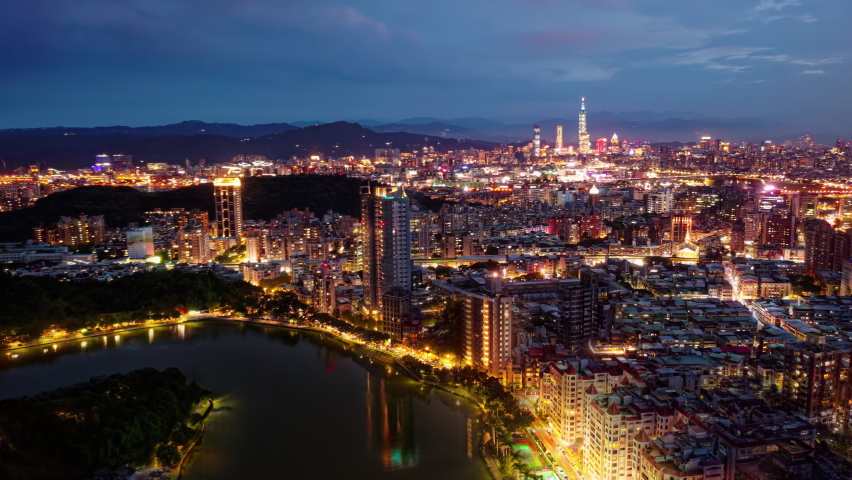 Aerial skyline of downtown Taipei, the capital city of Taiwan, viewed from above Bihu Park in Neihu District, with 101 Tower standing among skyscrapers in XinYi District from blue dusk to dark night