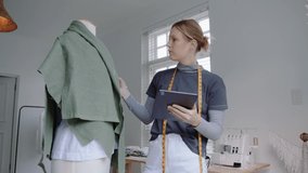 Caucasian female typing on digital tablet designing women's clothing in fashion studio