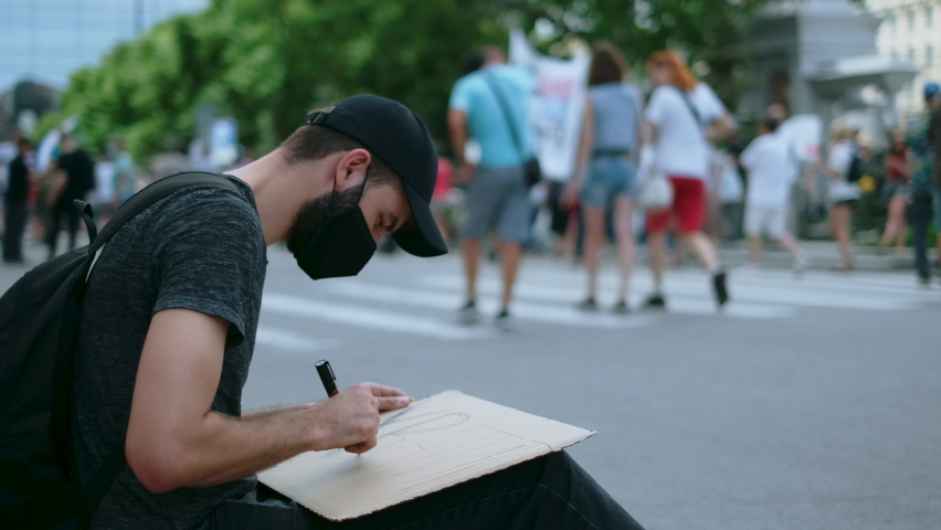 Peaceful protester man on political rally in covid-19 mask draws sign poster. Rebel man on city street revolt, resistance strike. Male picket activist drawing demonstration banner placard protesting. Royalty-Free Stock Footage #1078065038