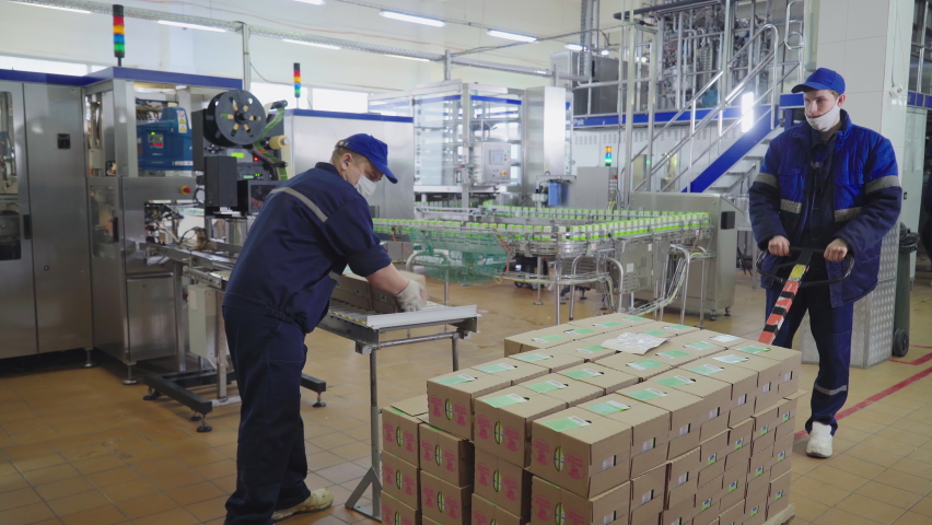 Factory worker is placing the packaged box in a stack. A Worker is moving the packaged boxes using the industrial cart. Worker is transporting the packaged boxes into the storage facility. Dairy food