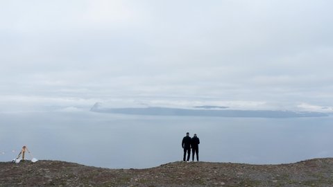 Tourists Standing At the Edge Of The Cliff Overlooking The Thick Fog Covering The Island In Westfjords, Iceland. aerial