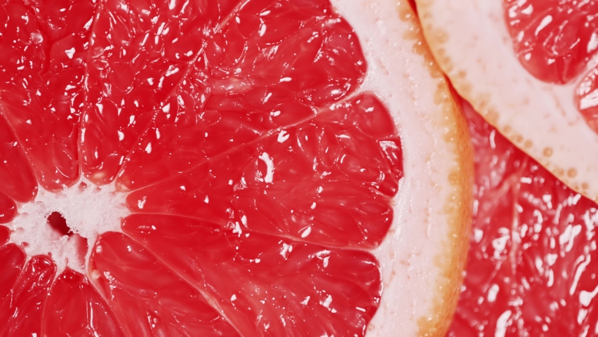 Slow motion of rotation ripe sliced grapefruites. Circles of fresh citrus as food background. Tropical fruits. Concept of proper nutrition or healthy lifestyle. Macro shot.