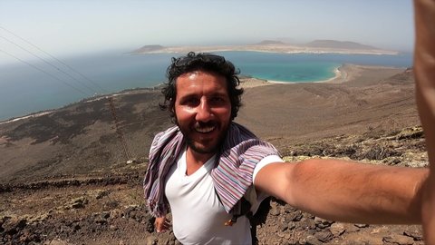 tourist is standing on the Lanzarote valley with red mountains in the national park Timanfaya in Lanzarote, Canary islands and taking selfie photo. slow motion