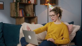 Young teenager woman in glasses celebrating birthday online, communicating with friends using laptop computer, sitting on sofa, female speaking with parents on video call in social media. 