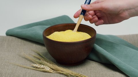 Falling polenta from wood spoon into bowl. Shooting of stirring cereal and groats in studio. Macro footage of pouring out the grits. Food cooking, harvest video. 