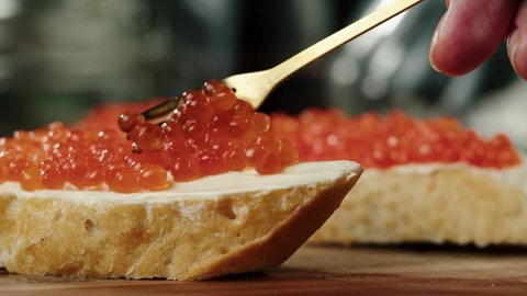 Putting red caviar on bread and butter, close-up of caviar sandwich. Salmon salted orange roe. Raw seafood. Luxury gourmet food. Delicious and tasty fish products. Russian cuisine.