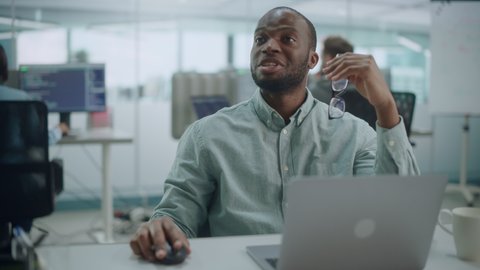 Modern Office: Portrait of Happy Black IT Programmer Working on Laptop, Talking, Brainstorming with Colleague. Male Software Engineer Wearing Glasses Develop App, Program, Video Game. Medium Shot