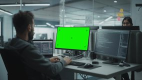 Multi-Ethnic Office: IT Programmer Working on Computer with Green Screen Chroma Key Display. Male Software Engineer Developing App, Program, Video Game. Terminal with Code Language. Over Shoulder Shot