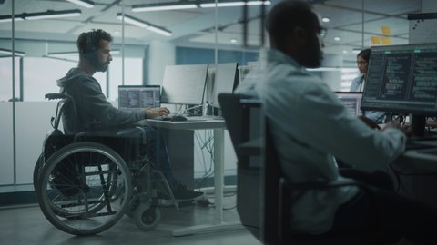 Disability-Friendly Office: Amazing IT Programmer with Disability in a Wheelchair Working on Desktop Computer. Male Specialist Create Inspirational Software. Engineer Develop Innovative App, Program