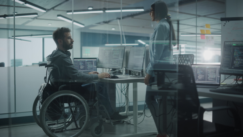 Disability-Friendly Office: Happy IT Programmer with Disability in a Wheelchair Talks with Colleague while Working on Computer. Software Engineers Develop Innovative App, Program. Medium Shot Royalty-Free Stock Footage #1078078115