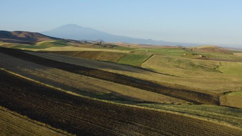 Drone shooting of the wheat fields in the heart of Sicily on the Erei mountains. Sicilian wheat cultivation. Small rural villages of Ramacca and Raddusa. Hay and grain. View of Etna.