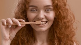 Red-Haired Woman With Ceramic Braces Brushing And Cleaning Teeth With Toothbrush Doing Oral Hygiene Routine Smiling To Camera Posing Over Beige Studio Background