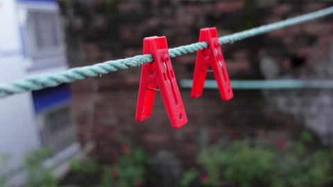 Two red clips hanging on a plastic rope. Clothespins on the rope. Red-colored plastic clothespins on a rope in the environment background. A row of red clothes clips. 4k video.