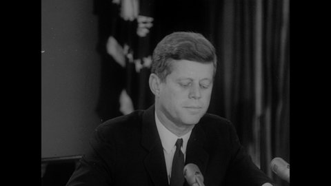 1960s: President John F. Kennedy delivering speech into microphones.