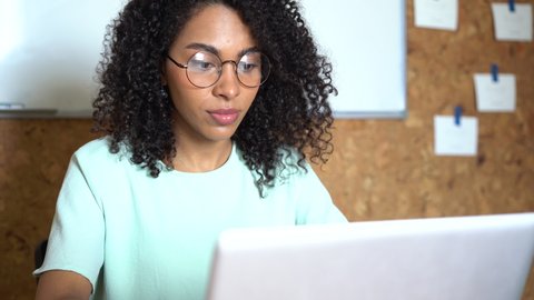 Thinking mixed-race businesswoman working on laptop computer in office interior