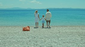 Happy family walking on the beach with their blond-haired little girl. Happy family enjoying vacation. Slow motion video. 