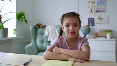 Home distance schooling for kids. Spbd Happy little girl with mole on cheek nods head and talks at videochat at table in children room camera view