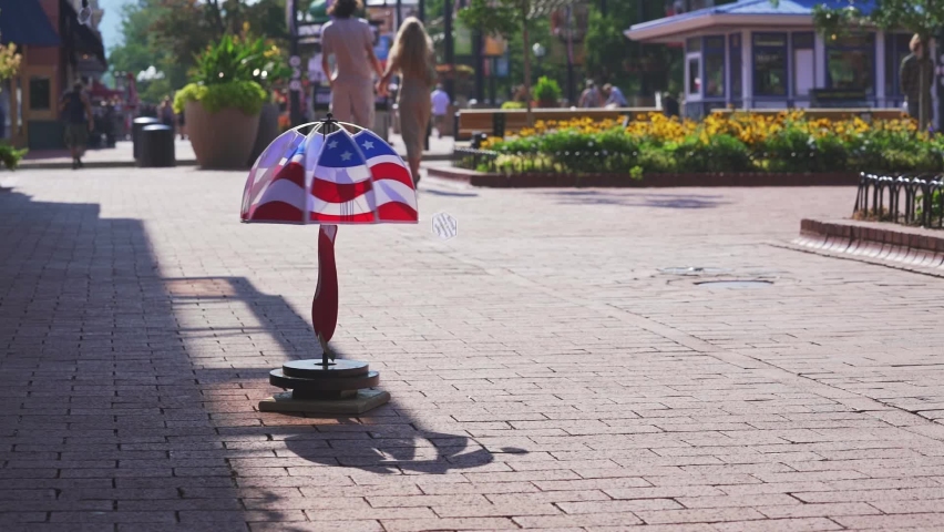 An American Flag whirligig spinning in the wind in slow motion as a young couple walks by on Pearl Street in Boulder Colorado