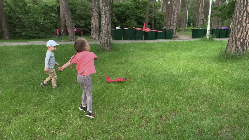 Three happy preschool toddler siblings children friends kids running around have fun in summer park playing on meadow hold toy airplanes launching fly into sky. Childhood, friendship, rest, nature