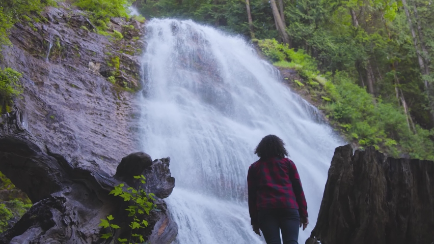 Woman watching the Waterfall in the Canadian rainforest. Bridal Veil Falls Provincial Park near Chilliwack, East of Vancouver, British Columbia, Canada. Nature Background. Slow Motion
