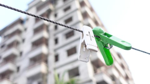 White and green two cloth fastening clips are hanging on a plastic rope. Clothespins on the rope. Plastic clothespins on a rope in the high res building and sky background. 4k video.