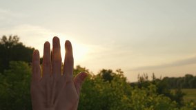 4k slow motion video of female hand isolated on sunny sunset sky background. Sun shine bursting and sparkling with magic rays and beams among fingers of hand of woman