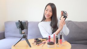 A young beautiful woman in front of a smartphone in video mode is in the middle of a social media makeup tutorial.