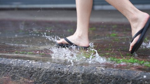 A flipflops feet running on the paving footpath on raining day, on the street side walk, flooding street, with rain and water, lower body part, rush hurry run finding the shelter to hide the rain
